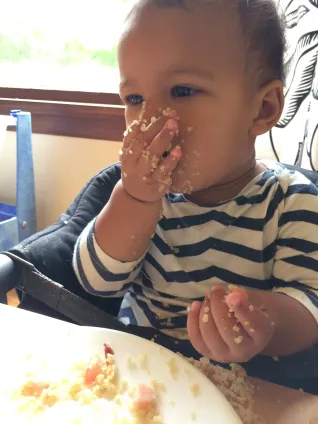 A toddler in a high chair feeding themselves
