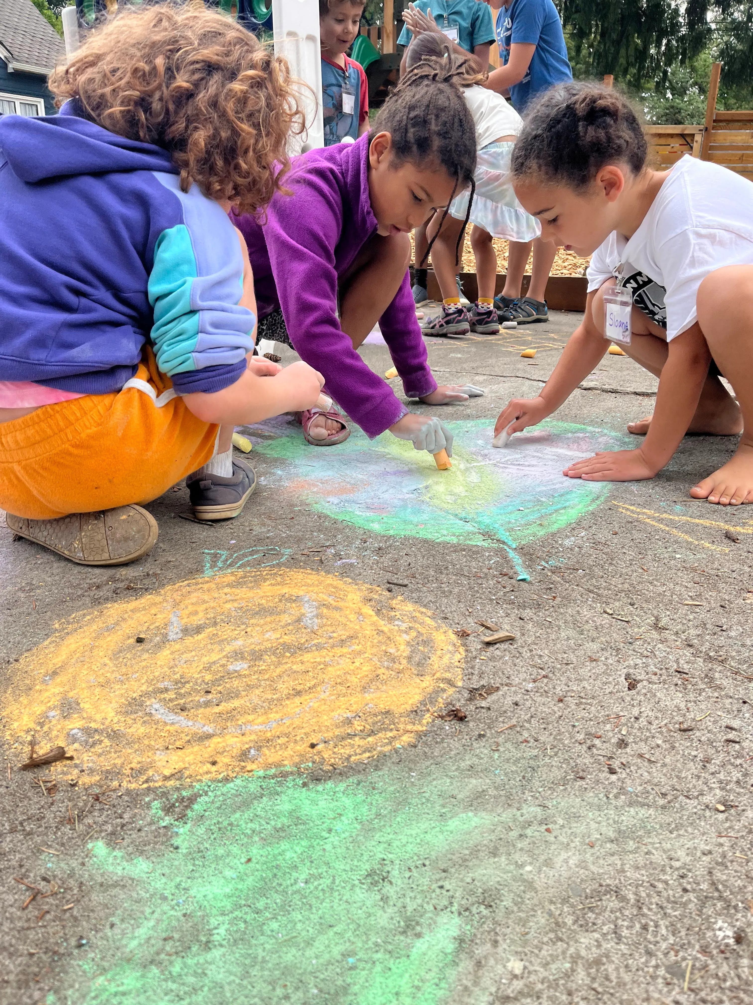 Campers deeply focused together on a collaborative sidewalk chalk drawing