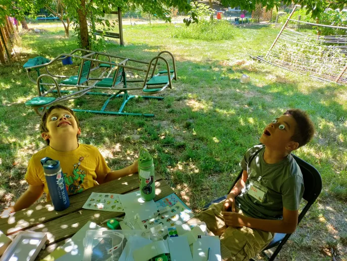 Two campers laughing outside with googly-eye stickers stuck to their faces